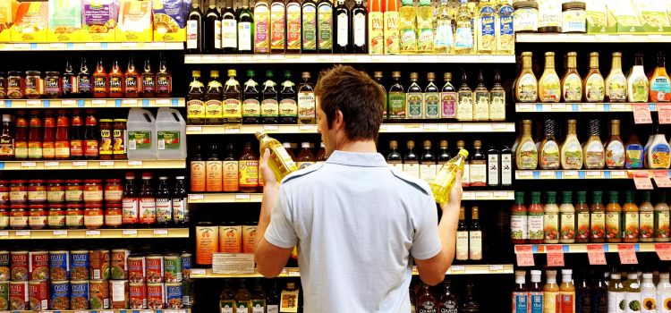 A man stands in front of a grocery store aisle and compares bottles in each hand