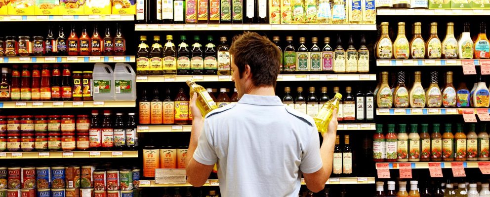 A man stands in front of a grocery store aisle and compares bottles in each hand