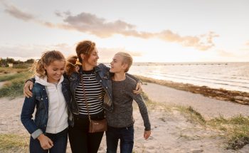 A mom and her two kids walk along the beach.
