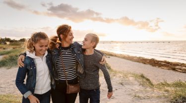 A mom and her two kids walk along the beach.