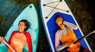 2 women on lie on paddle boards looking up and laughning