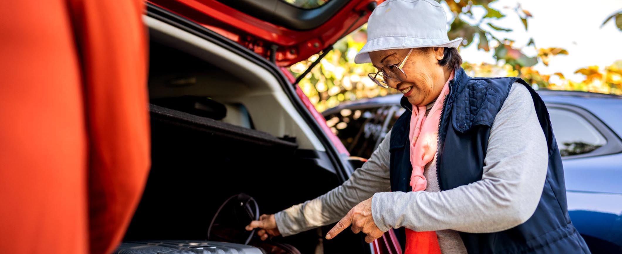 Senior woman unpacking luggage from a car trunk outdoors