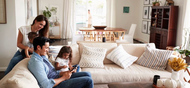 Man and woman with their two children looking at an iPad on their couch.