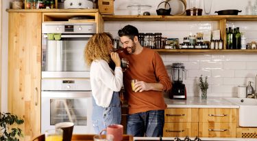 Couple drinking coffee and laughing in their kitchen.