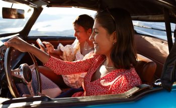 Woman driving a car while another woman sits in the passenger seat on her phone.