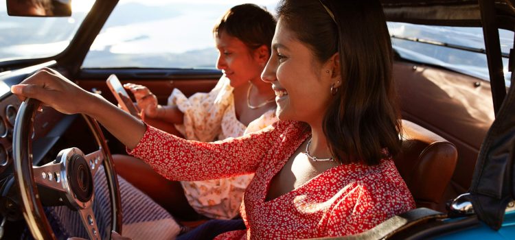 Woman driving a car while another woman sits in the passenger seat on her phone.