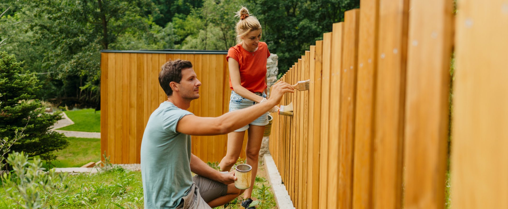 A man and woman paint a fence in their yard.