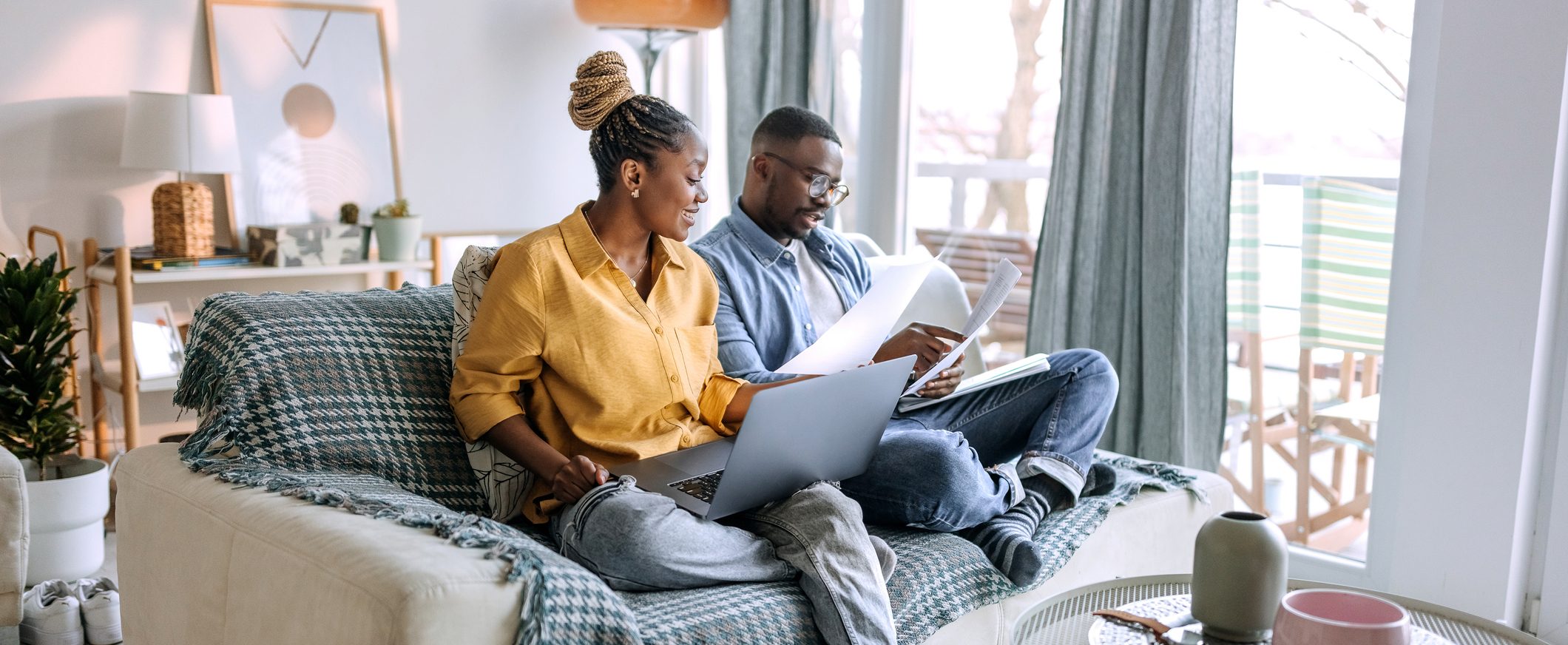 A couple sit on a couch with a laptop and look over documents.