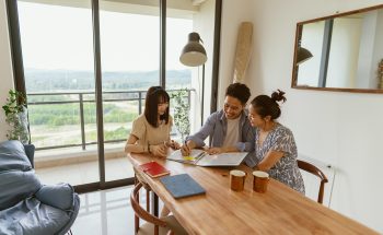 3 people sit at a dining room table and look over documents.