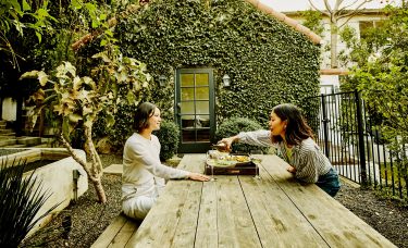 Two friends enjoy wine and salads at an outdoor garden table.