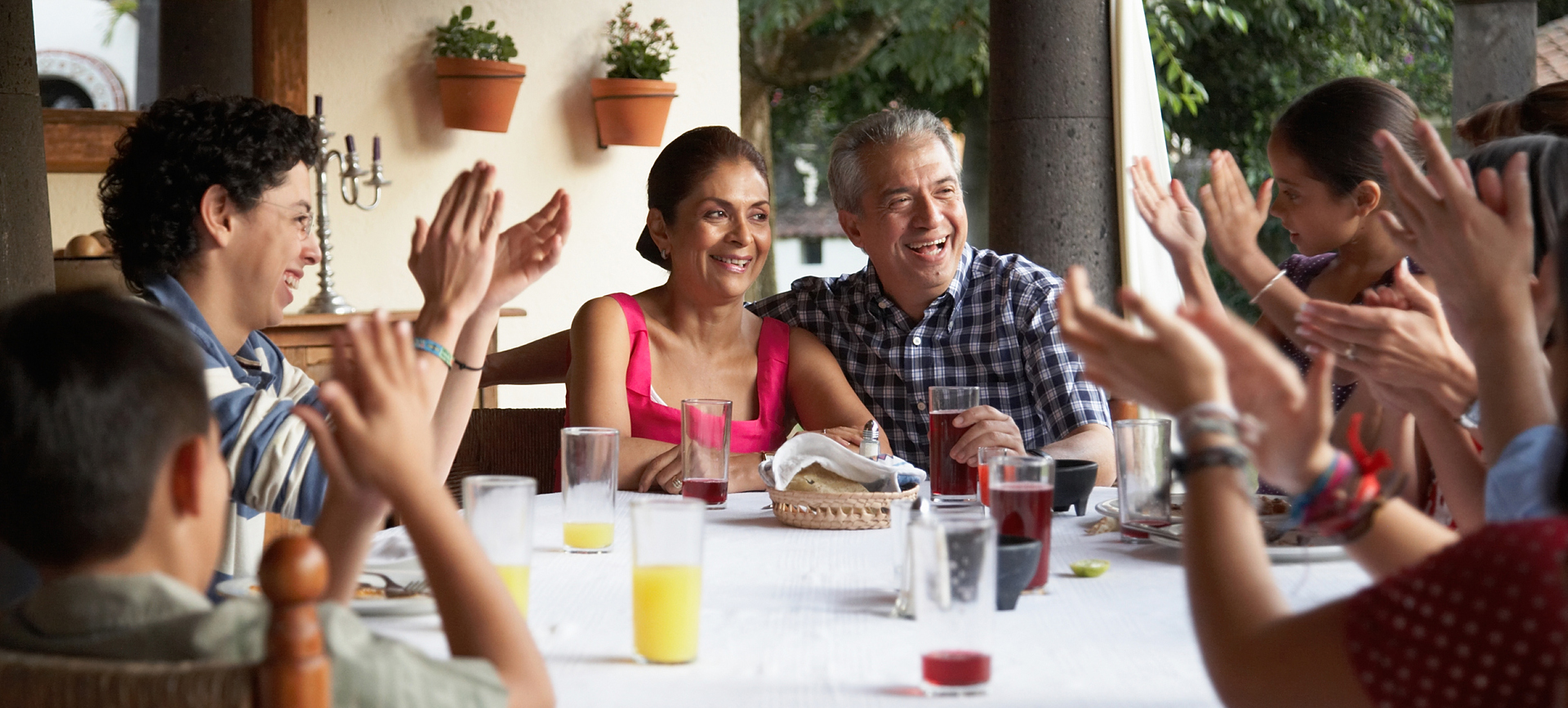 A family gathers around a table in a restaurant and claps for the couple at the center.