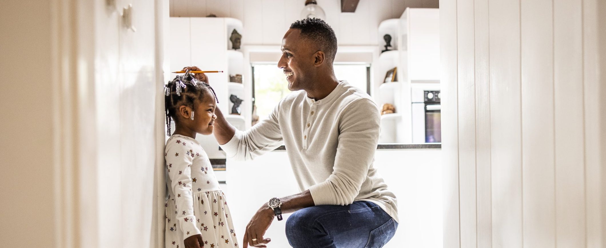 A father measures his daughter’s height on the wall behind her.