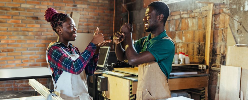 A man and woman use sign language in their workshop.