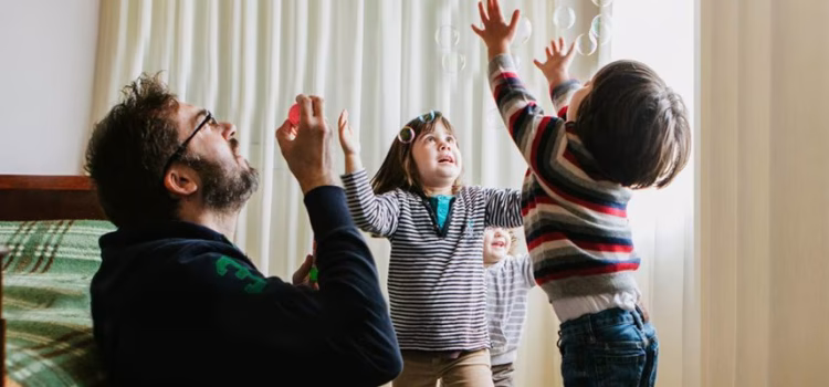 A dad blows bubbles while playing with his 2 kids