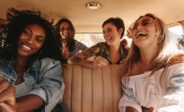 Four female friends smile and laugh during a road trip.