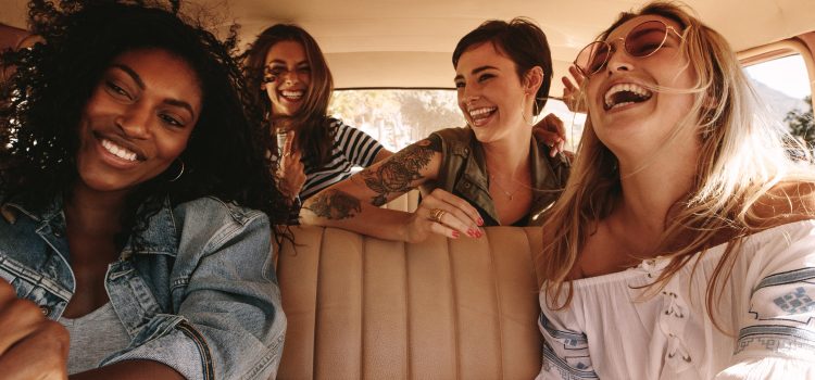Four female friends smile and laugh during a road trip.