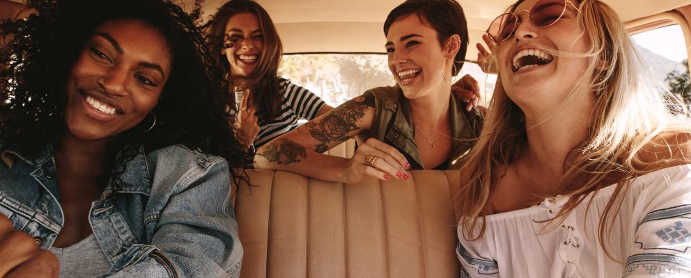 Four female friends smile and laugh during a road trip.