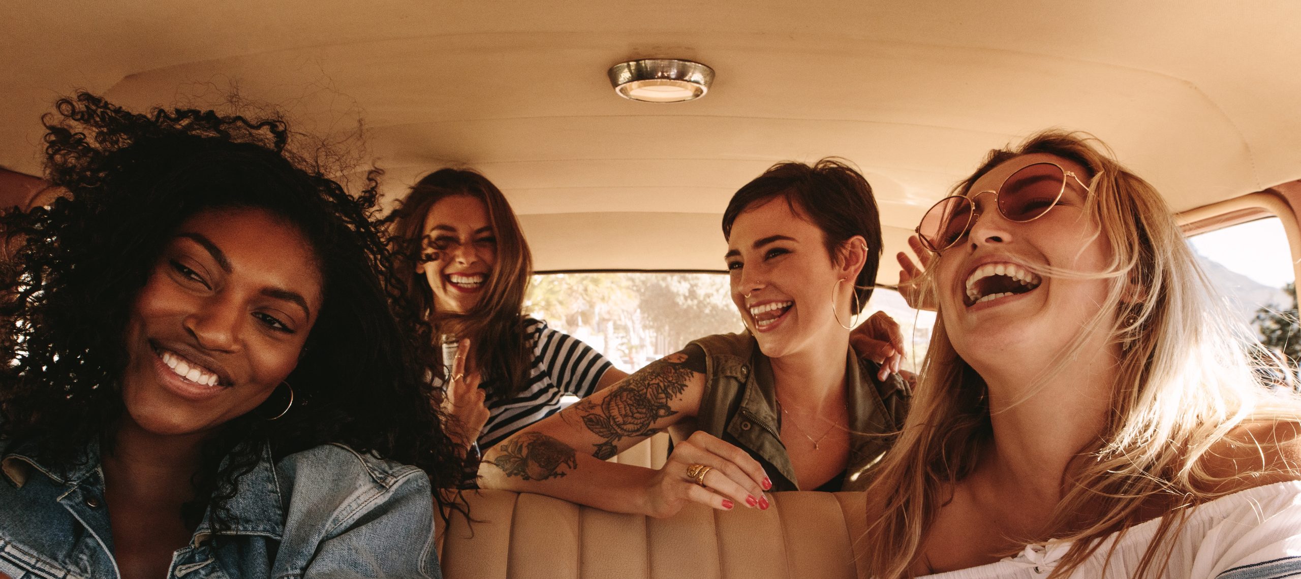Four female friends smile and laugh during a road trip.