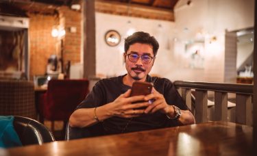 A young man sits and looks at his phone.