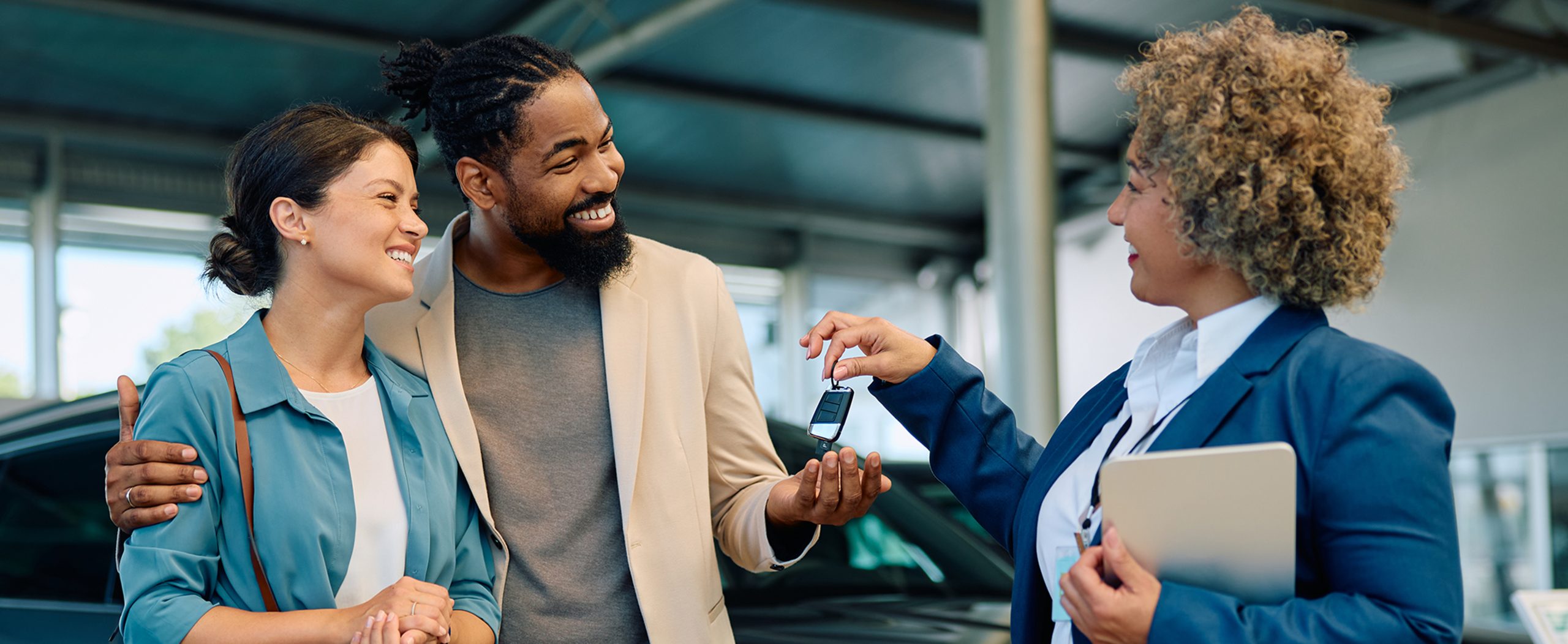 A couple smiles as they receive keys to a car in a garage.