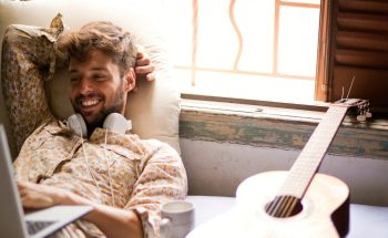 Man with headphones around his neck smiling at his computer.