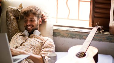 Man with headphones around his neck smiling at his computer.