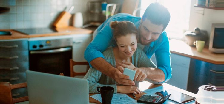 Couple looking at a mobile phone while reviewing paperwork in their kitchen