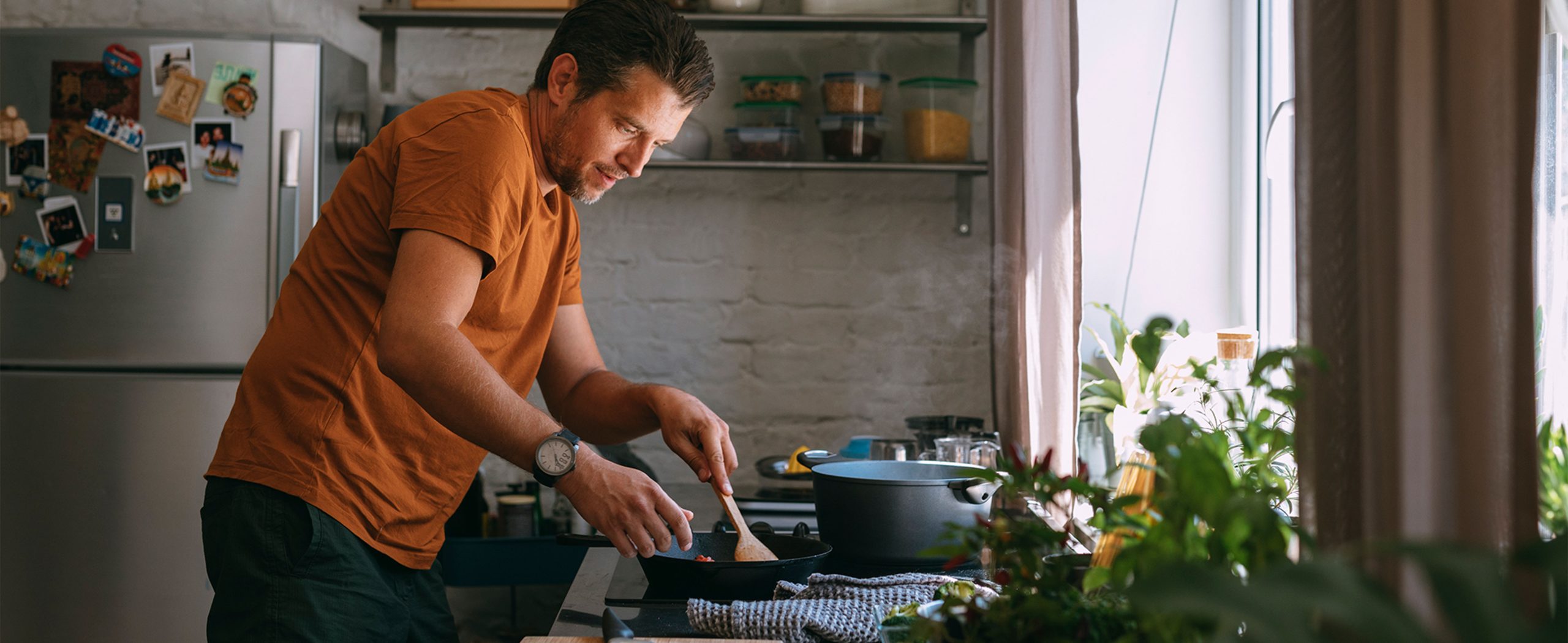 A man cooks in his kitchen with a wooden spoon.