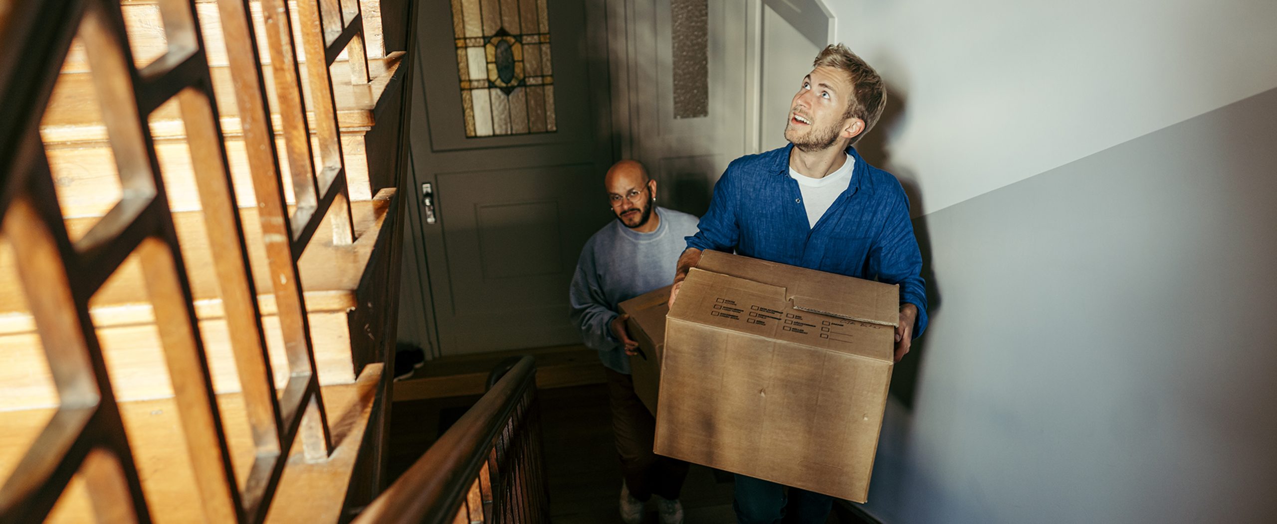 Two men carry moving boxes up the stairs.