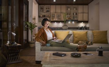 A woman relaxes on a sofa with a cup of coffee and her laptop.