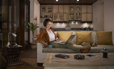 A woman relaxes on a sofa with a cup of coffee and her laptop.