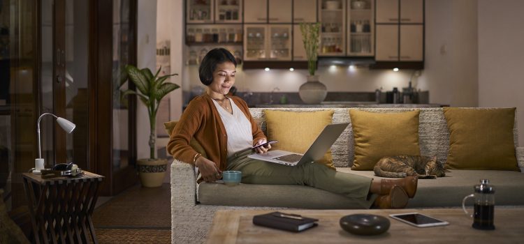 A woman relaxes on a sofa with a cup of coffee and her laptop.