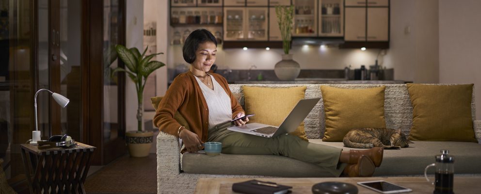 A woman relaxes on a sofa with a cup of coffee and her laptop.