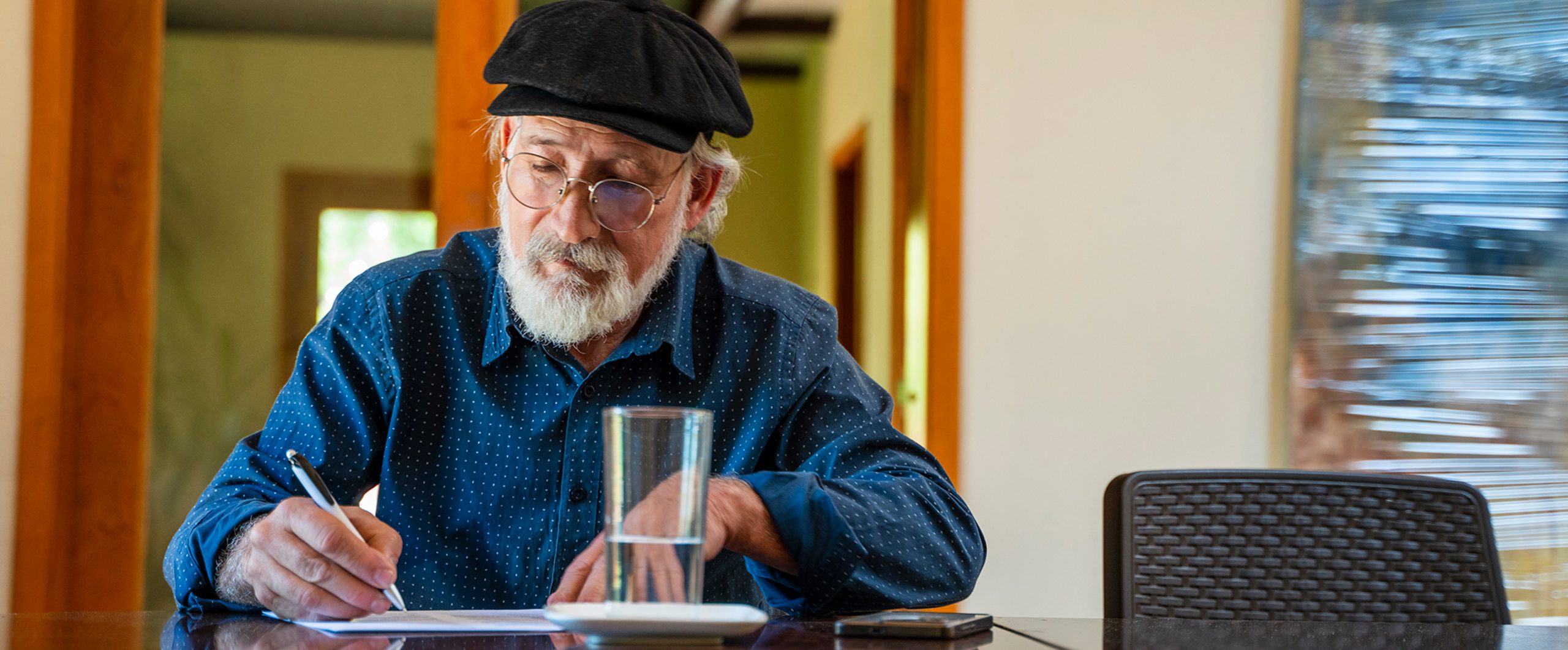 A man fills out paperwork at a table next to a glass of water.