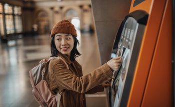 A young woman wearing a backpack uses an ATM.