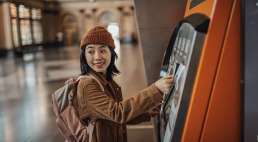 A young woman wearing a backpack uses an ATM.