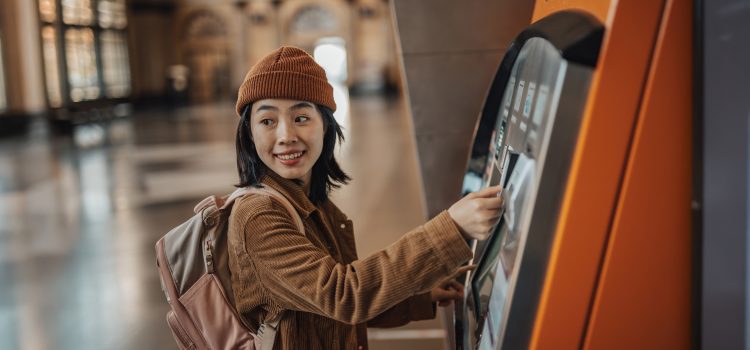 A young woman wearing a backpack uses an ATM.