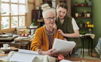 A woman and her granddaughter review documents together at a dining table.