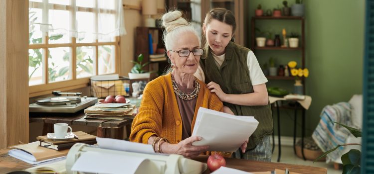 A woman and her granddaughter review documents together at a dining table.