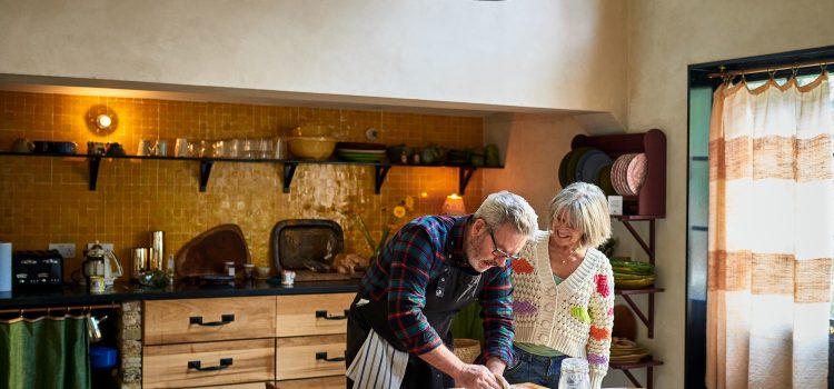 A retired couple roll out bread dough together on their dining table.