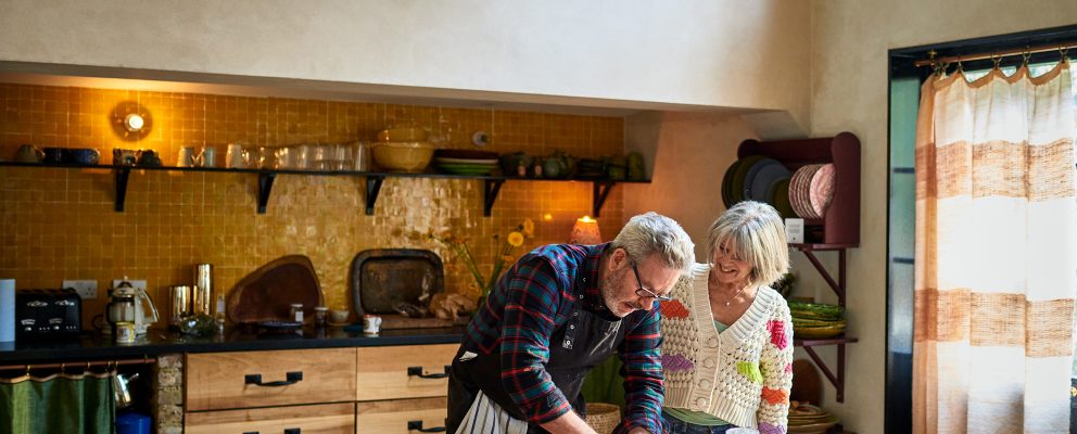 A retired couple roll out bread dough together on their dining table.
