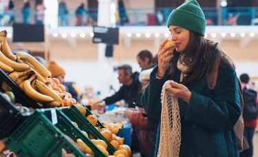 A young woman sniffing a piece of fruit at a grocery store.