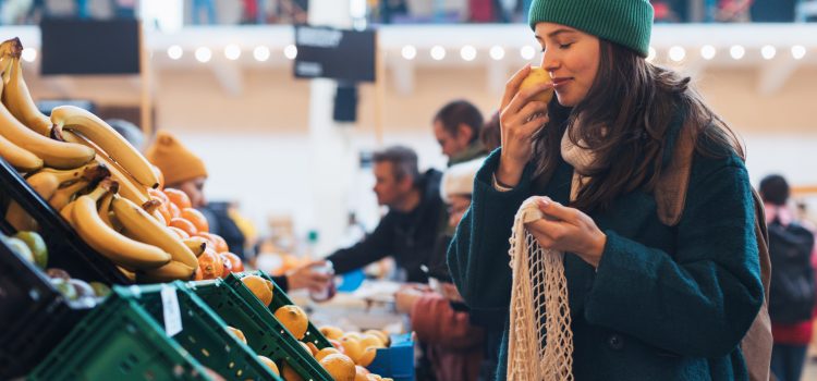 A young woman sniffing a piece of fruit at a grocery store.