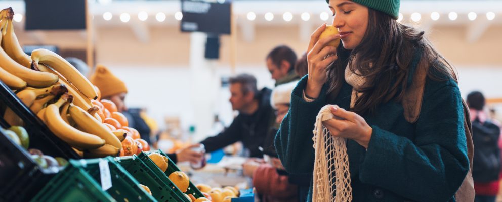A young woman sniffing a piece of fruit at a grocery store.
