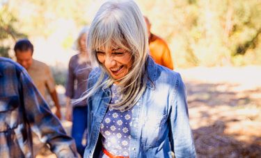 A retired woman smiling and walking through the woods with people.