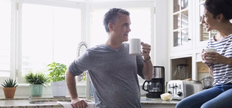 Husband and wife talking in their kitchen while enjoying a cup of coffee.