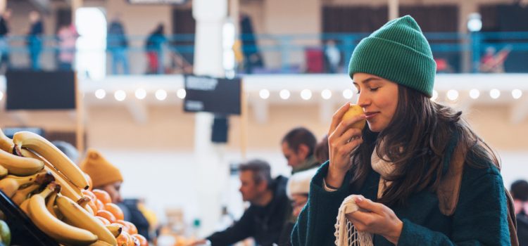 A young woman sniffing a piece of fruit at a grocery store.