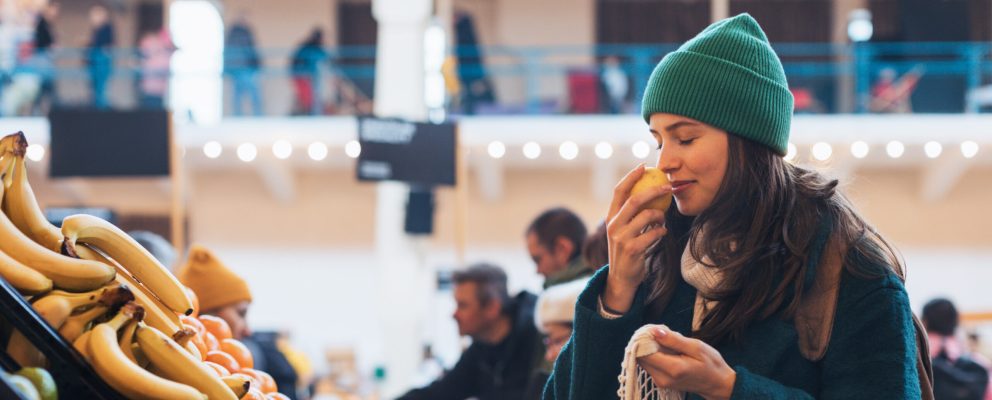 A young woman sniffing a piece of fruit at a grocery store.