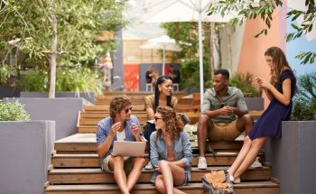 Group of friends sit on stairs outside while hanging out and talking