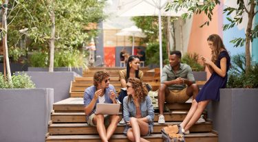 Group of friends sit on stairs outside while hanging out and talking